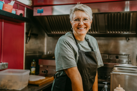 A woman with short gray hair dressed in an apron in a kitchen