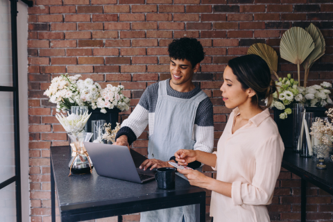 A young woman and young man in a flower shop working on a computer