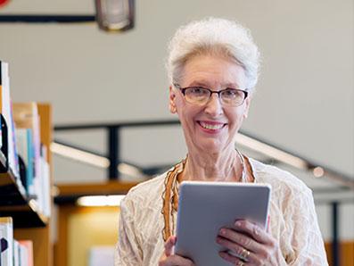 An older woman holding a tablet next to a bookshelf